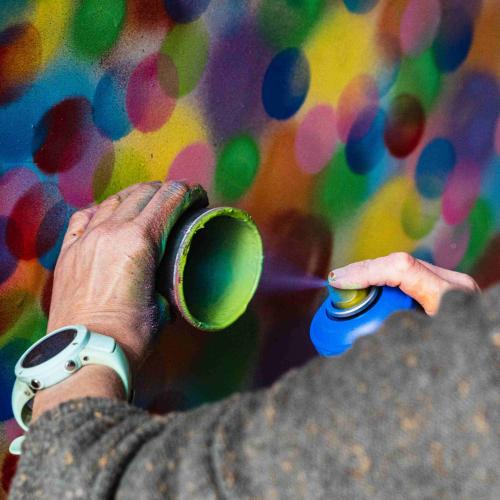 Close up of someone's hands spray colourful circles onto a board