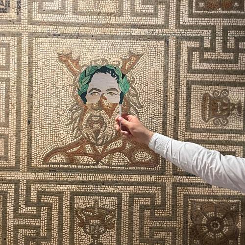 Decorated paper mask held in front of mosaic