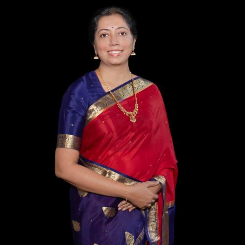 A posed portrait of a lady with Indian heritage wearing a saree and gold necklace