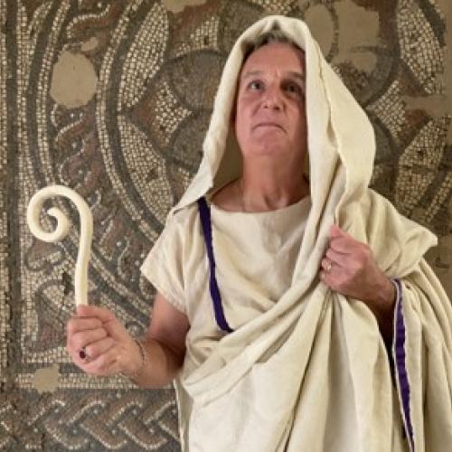 Man dressed as Roman priest in front of mosaic