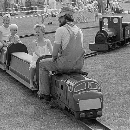 A man riding a tiny train with two children on the carriages