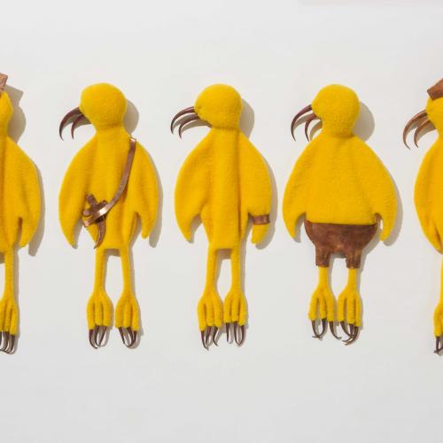 Yellow Birds, five yellow cartoon-like birds made of fleece and laid down next to one another with their head facing left, each featuring a fabric accessory such as hats, shorts, a bag, and hair tied in a bun