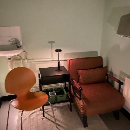 A small room with two chairs and a table with a lamp. You can see a sink on the wall.