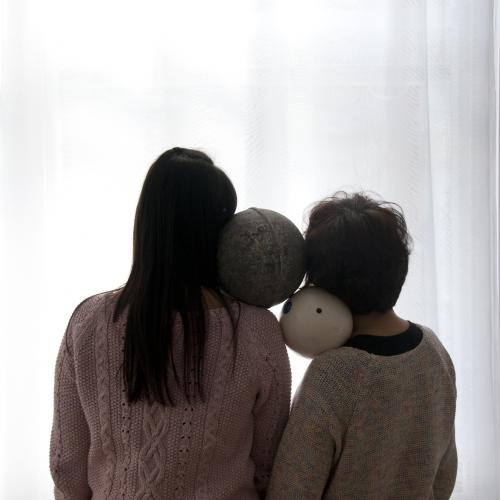 Two Buoys Two Voids, photograph showing the back of two people standing close in front of a bright white screen and holding two buoys on their shoulder.