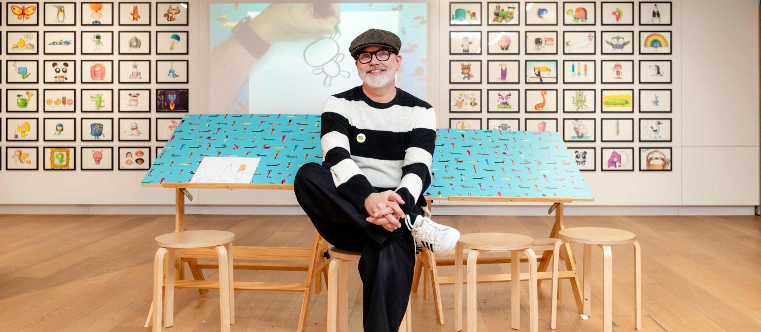 Rob Biddulph sitting in an exhibition of his work
