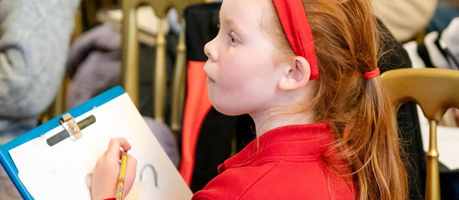 child in red drawing on clipboard