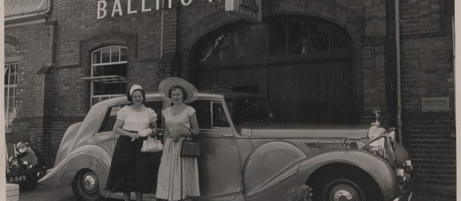 Two women standing in front of a car, in front of the Ballito factory.