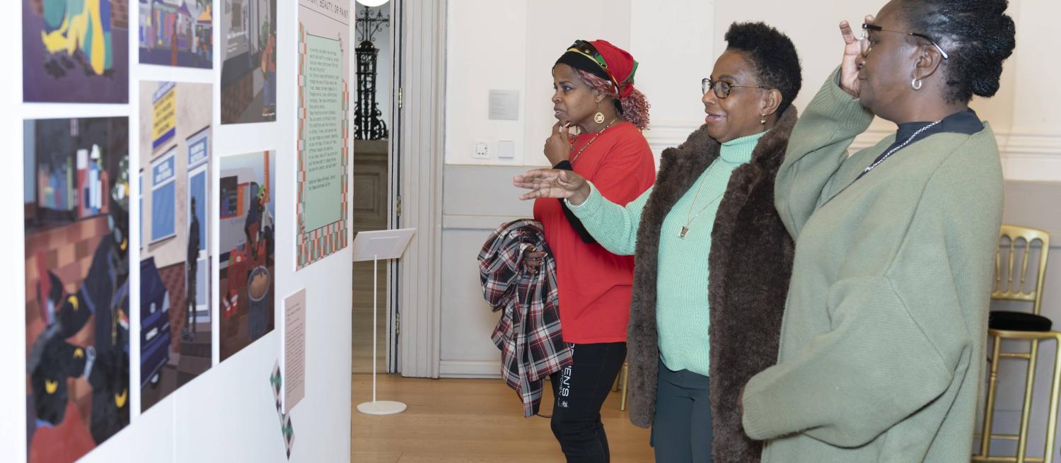Three women looking at an exhibition of historical research and art. They gesture towards it and one of them is speaking.