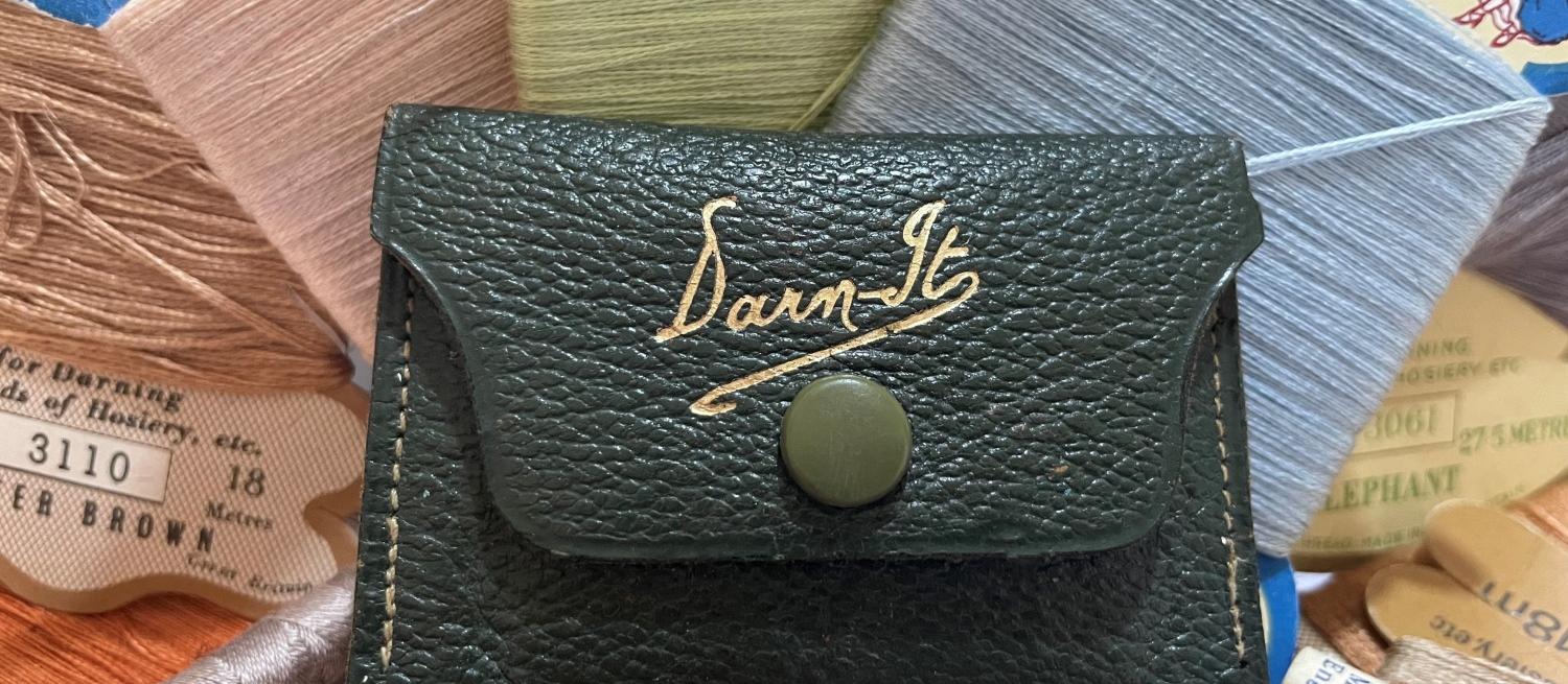 Colour image of a small sewing case with 'darn it' printed on the front. In amongst a variety of spools of thread. 