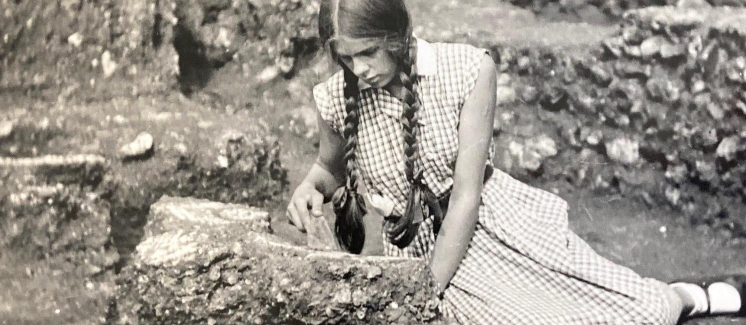 Black and white 1930s photograph of a teenage girl sitting on the ground and digging with a trowel