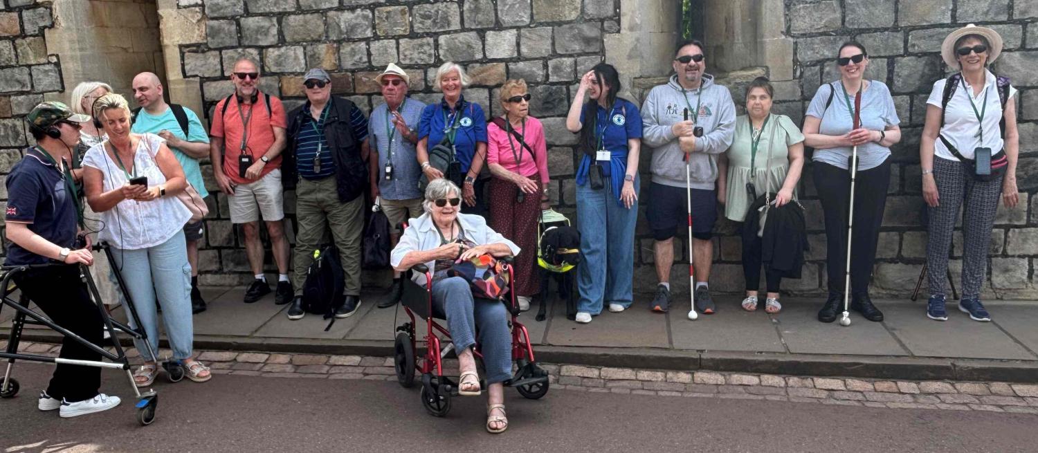 Photograph of members of Herts Vision Loss positioned in a line in front of a stone wall