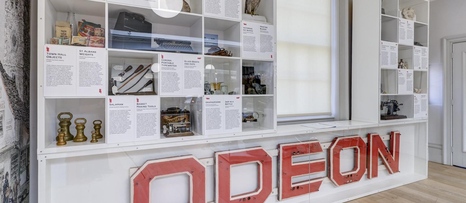 Museum display case containing large ODEON cinema sign, Victorian straw boater hat, peregrine falcon taxidermy and other museum collection ephemera