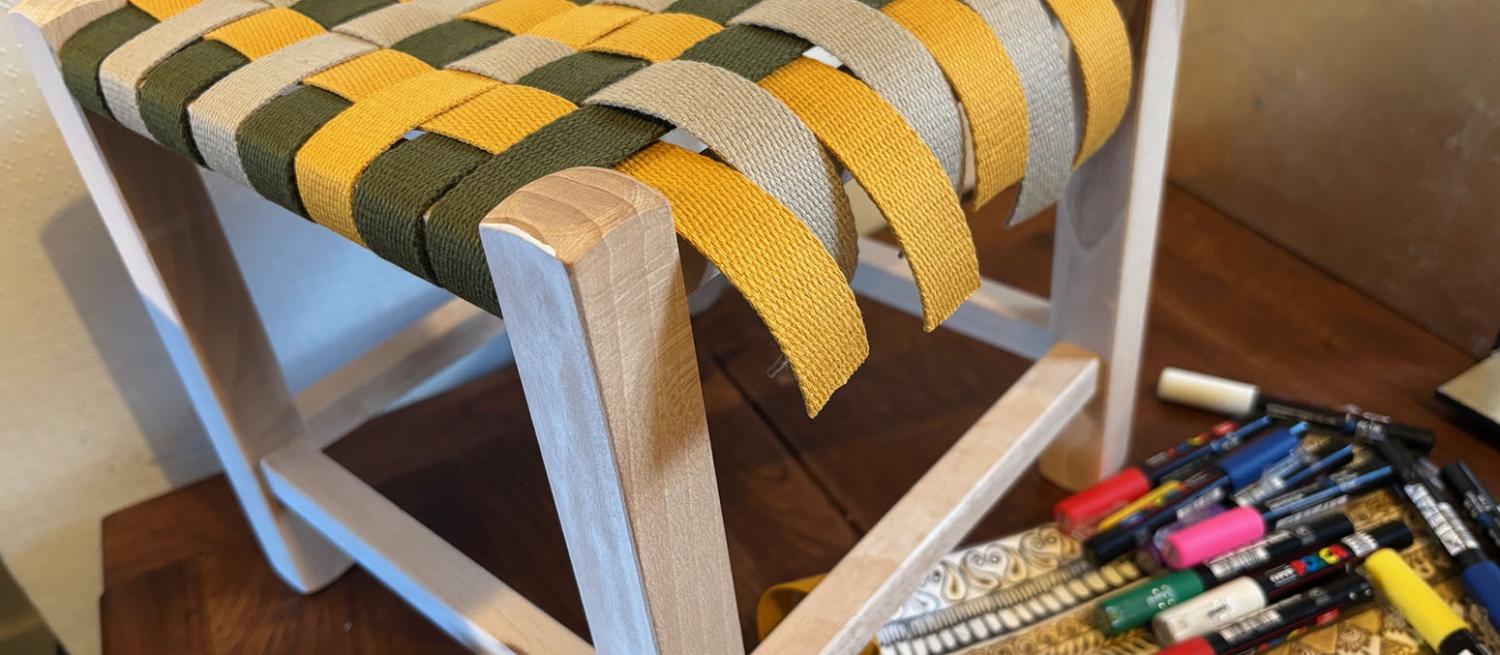 Colour photographic image of a small wooden stool frame with yellow and green woven top