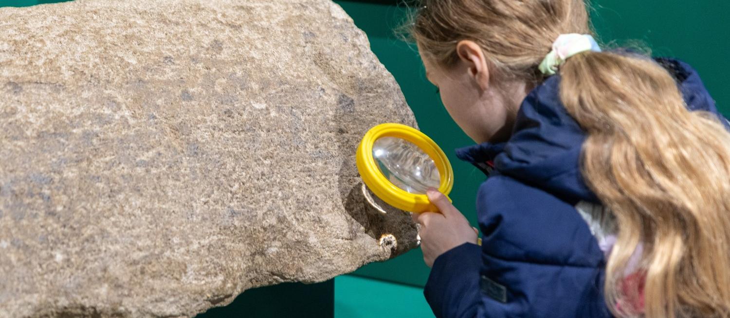 child examining stonework with magnifying glass