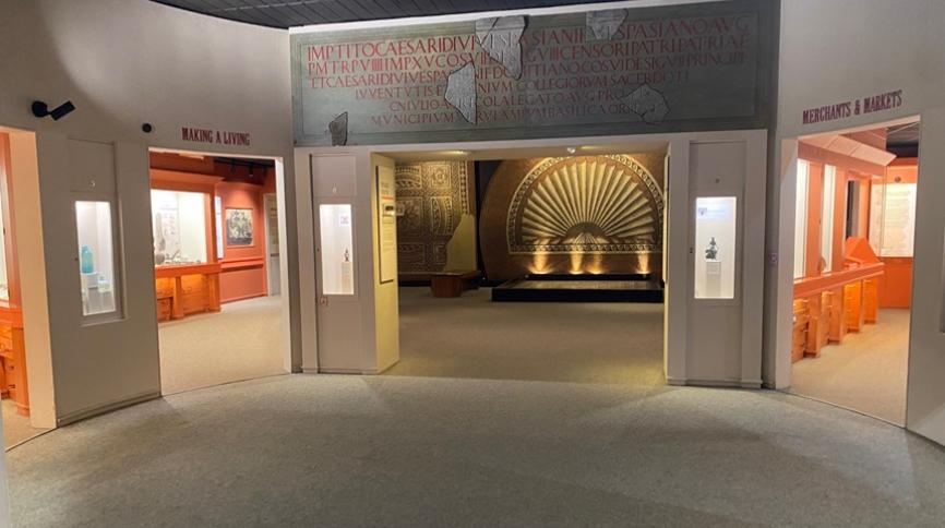 A large area with three doorways into more areas with display cases. Through the largest doorway, you can see large mosaics on the wall.