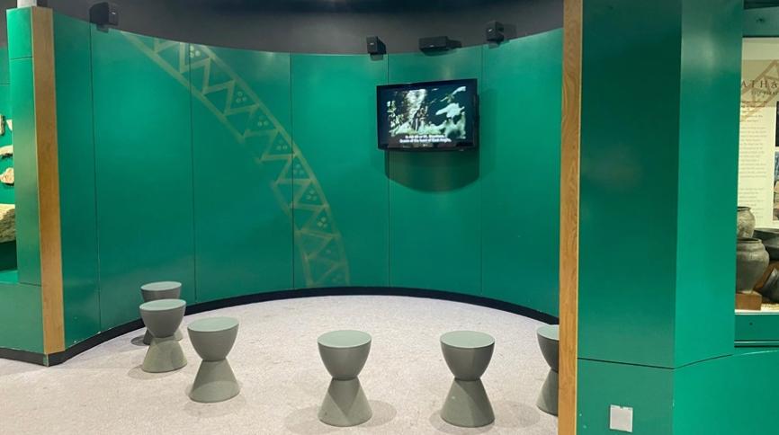 A nook with a TV high on the wall and stools in a circle in front of it.