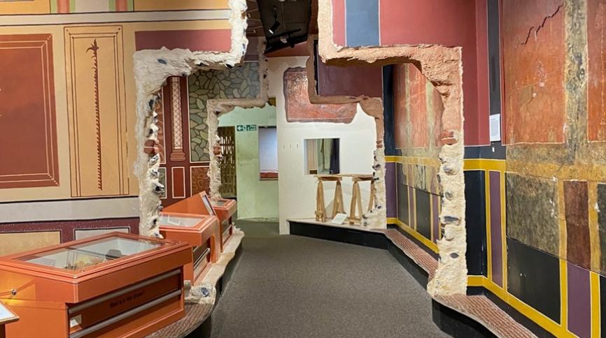 A long corridor with colourful painted walls on either side, and display cases with objects along the left hand side of the corridor.