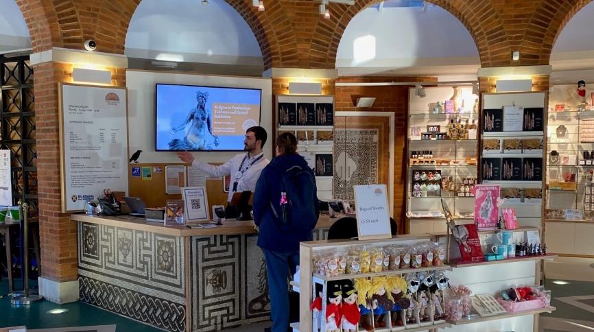 The inside of a shop where a staff member is serving a customer at the front desk.