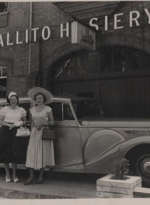 Two women standing in front of a car, in front of the Ballito factory.