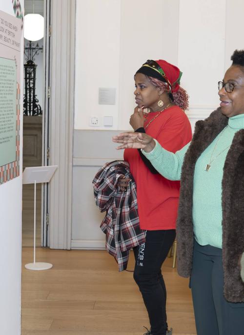 Three women looking at an exhibition of historical research and art. They gesture towards it and one of them is speaking.