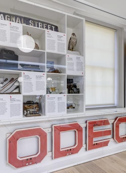 Museum display case containing large ODEON cinema sign, Victorian straw boater hat, peregrine falcon taxidermy and other museum collection ephemera
